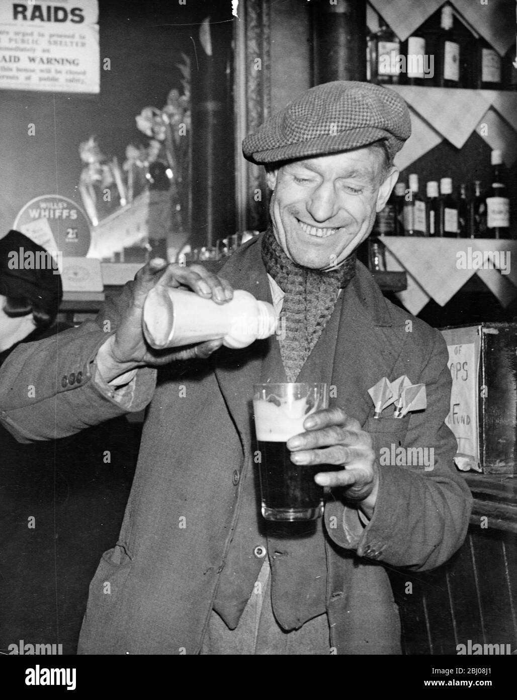 Man pours ground ginger in his pint of beer. As practised by stevedores and dockers during cold weather, ground ginger is found in many riverside inns near wharves, though elsewhere it is a rare relic of olden times. - Greenwich, Kent, England. - 15 January 1940 - Stock Photo