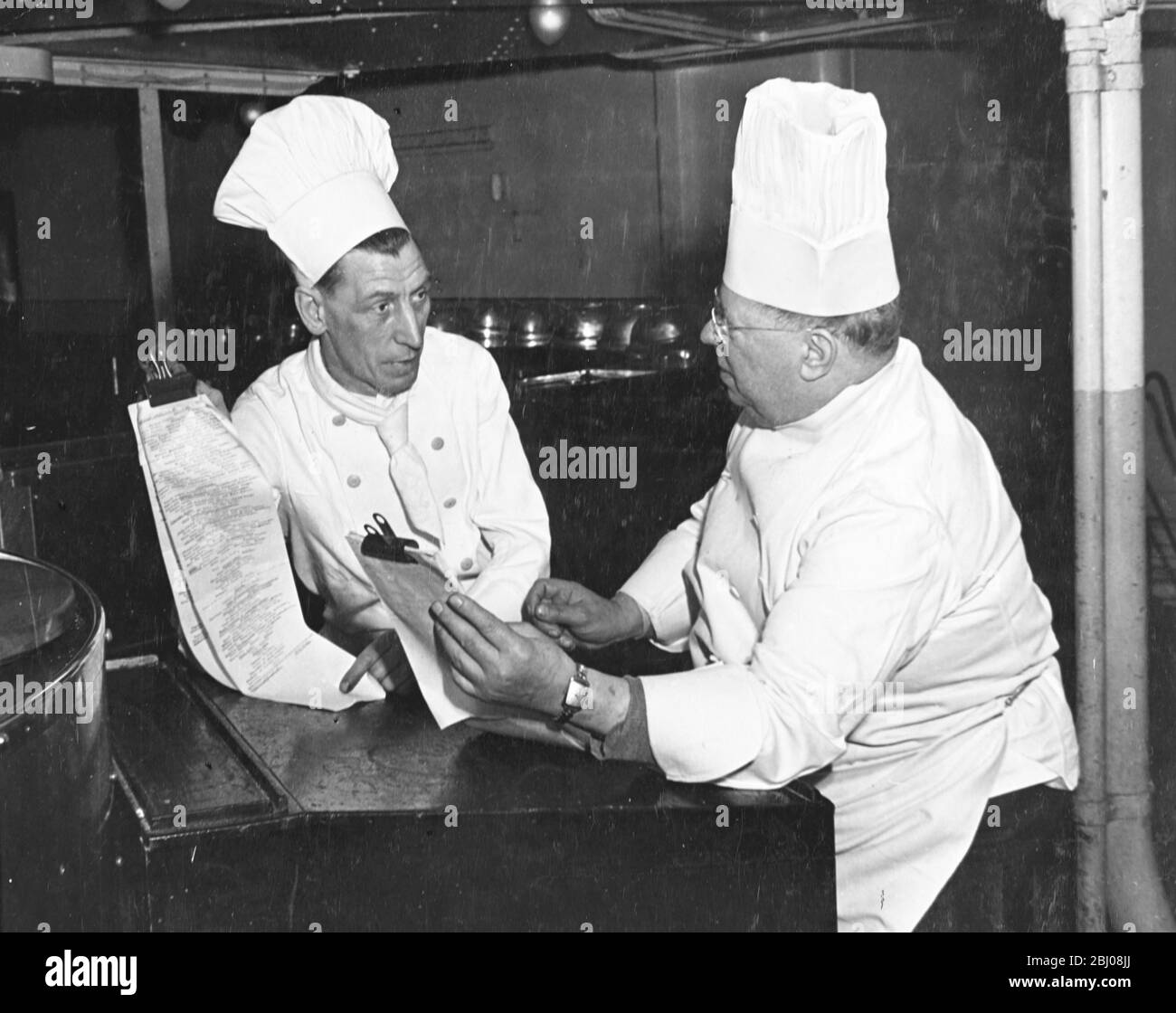 Queen Mary Chef Mr J. Pearce, assisted by second chef, Mr George Thomas (left) goes over a pre-austerity menu as new and reconditioned British liners re-establish their place in the North Atlantic. - Southampton, Hampshire, England bound for New York, USA. - 17 April 1948 Stock Photo