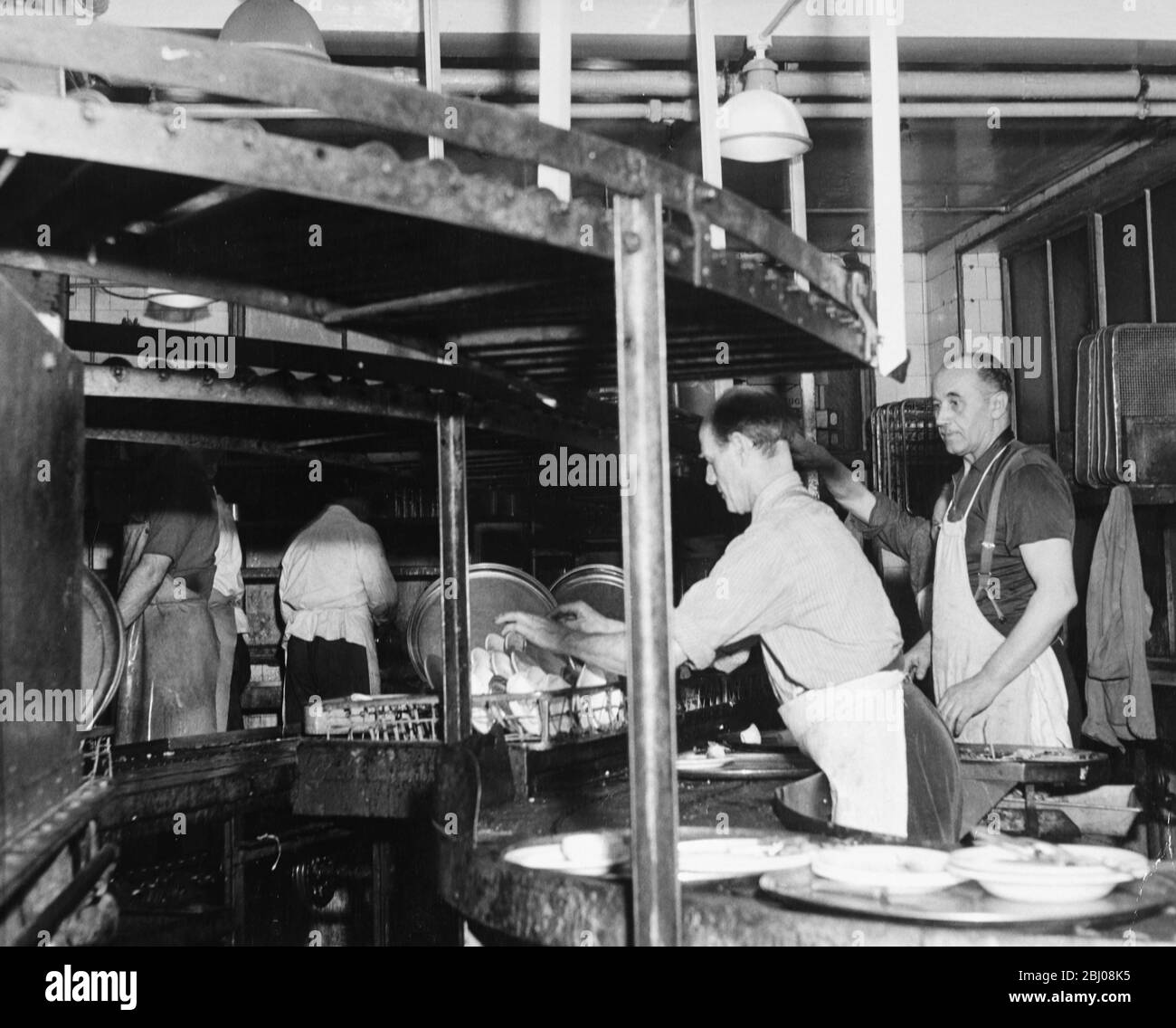 Deep below the kitchens the endless conveyors bring endless quantities of dirty dishes for the 'pearl divers', as the dishwashers are called, to wash up. - undated Stock Photo