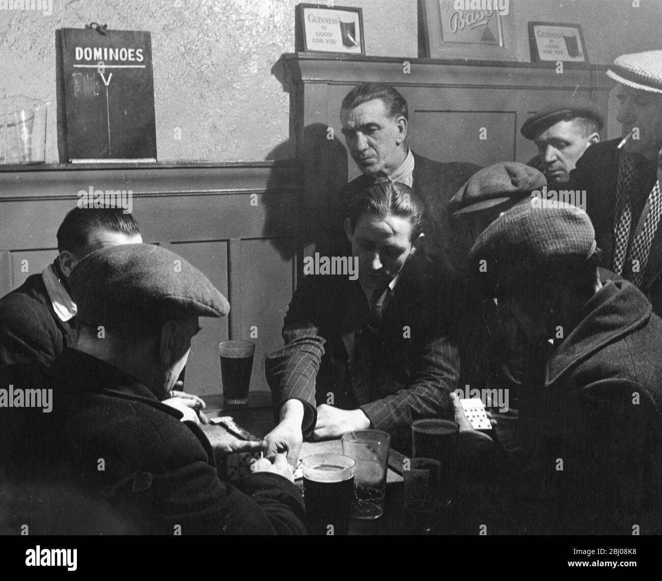 The Cosy Corner pub, a favourite with fruit market porters in Glasgow, Scotland. Male customers drink beer and play dominoes. - 1949 Stock Photo