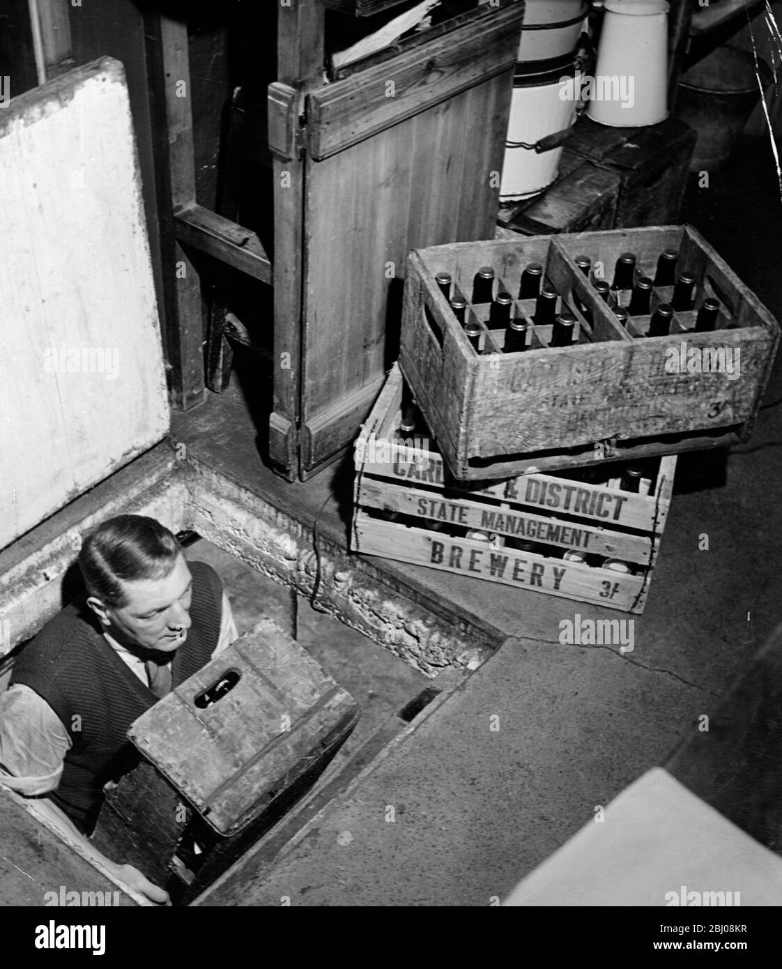 Joe, the landlord, brings up bottles of beer from the cellar to sell at the Globe Tavern. A state owned pub in Longtown, Carlisle, Cumbria, England. - December 1948 Stock Photo