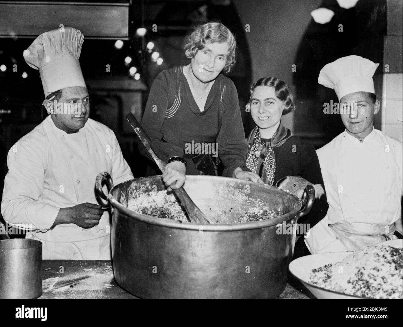 The Lady Mayoress, Lady Vincent assisted by her daughter, Mrs J Stephens and the kitchen chefs, stirring the mixture for the Mansion House Christmas puddings. - 12 December 1935 Stock Photo