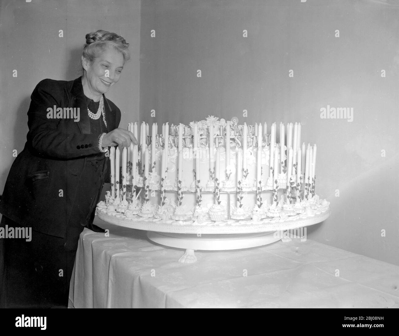 Britian, London: Hungarian-born Madam Maria Floris, managing director of a West End Bakery, with one of the cakes she designed with her husband for Sir Winston Churchill's 80th birthday. The cake has eighty candles and is 40 inches high; It weighs on hundredweight. The width of the door at number 10 Downing Street was measured to ensure the cake would go through. It will be delivered tonight. and tomorrow night it will be sampled by Sir Winston and 150 friends and relatives. - 29 November 1954 Stock Photo