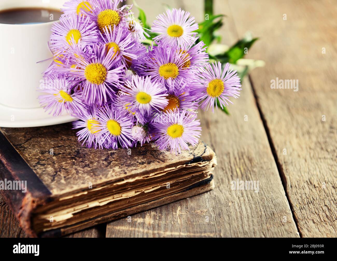 Old book with beautiful flowers and cup of tea on wooden table close up Stock Photo