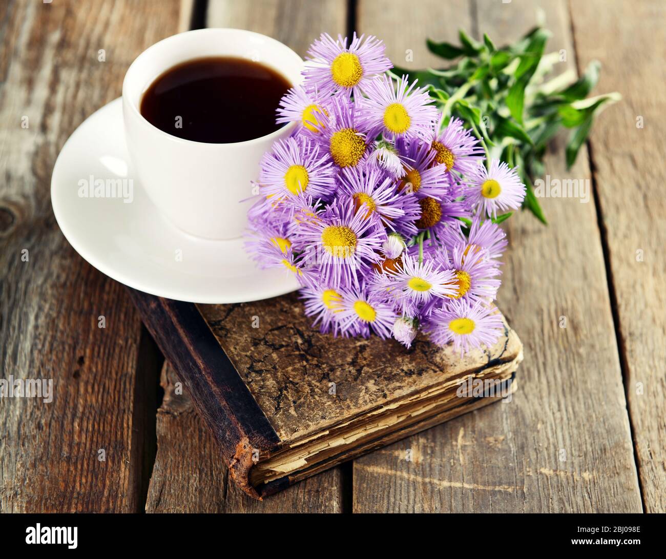 Old book with beautiful flowers and cup of tea on wooden table close up Stock Photo