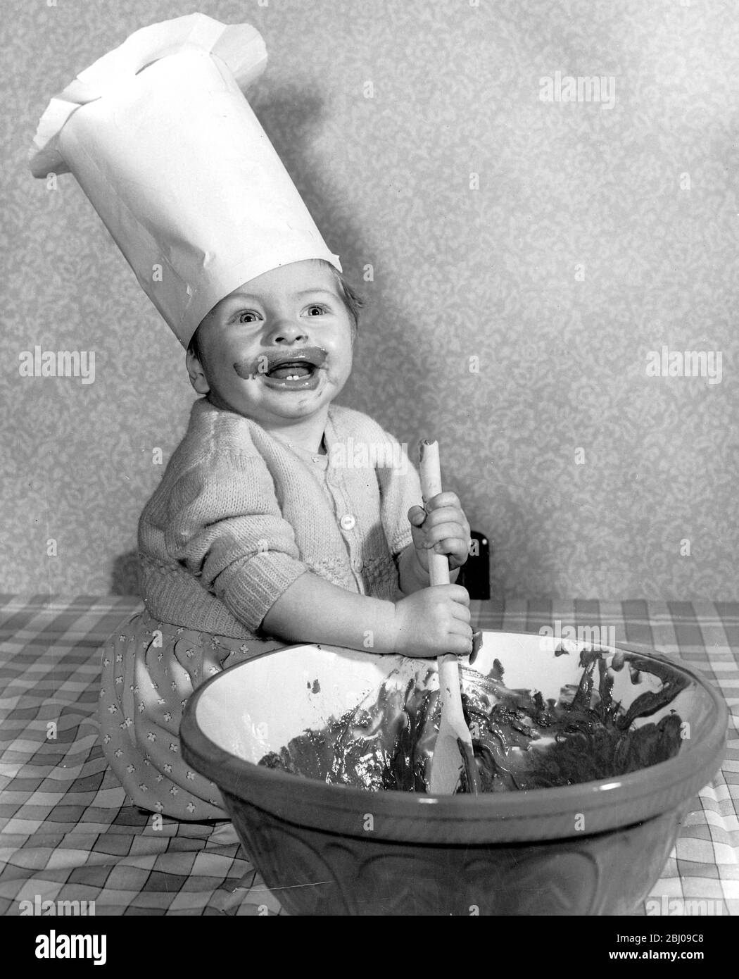 Eight months old Peter Raven of Bishop's Stortford takes a hand in the mixing of the Christmas pudding 1957 Stock Photo