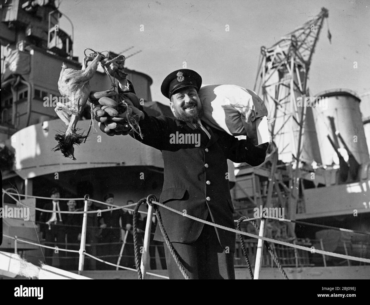 England Home and Booty. - Chief Petty Officer Alec Noble of Portsmouth comes ashore from the cruiser HMS Devonshire (39) with a clutch of bananas and a turkey. His wife and five daughters are assured of a happy Christmas. HMS Devonshire, Dr Plymouth on 30 November (Friday) . After a long cruising the Pacific. - 1 December 1945 Stock Photo