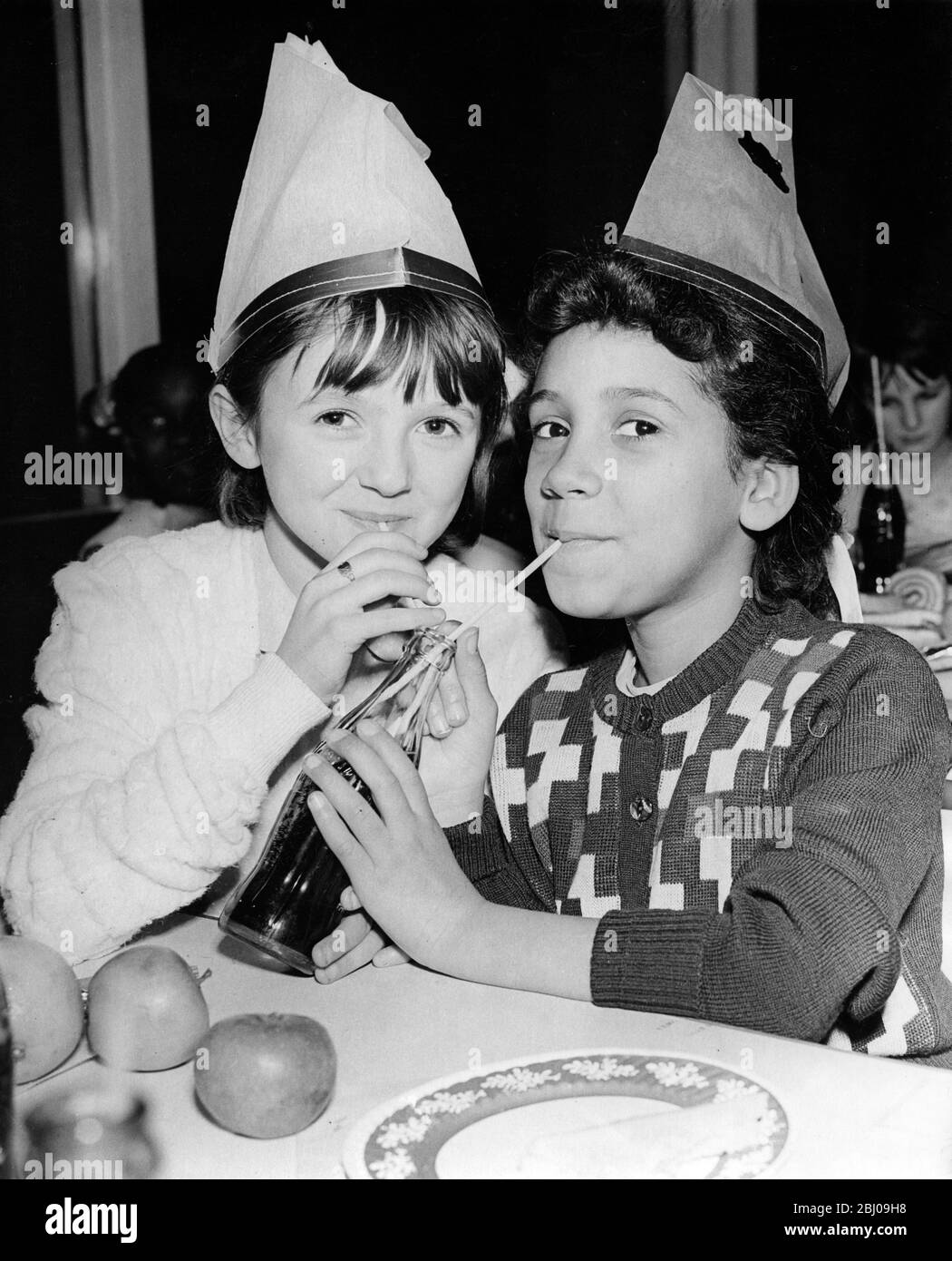 Young girls ( Valerie May and Kathleen Fenton ) share a bottle of Coca Cola between them at the Grand Children's Christmas Party at Holland Park Comprehensive School, Airlic Gardens, Campden Hill. Arranged by local people of many nationalities (especially West Indians) to help play a more active part in the community. - 24 December 1958 Stock Photo