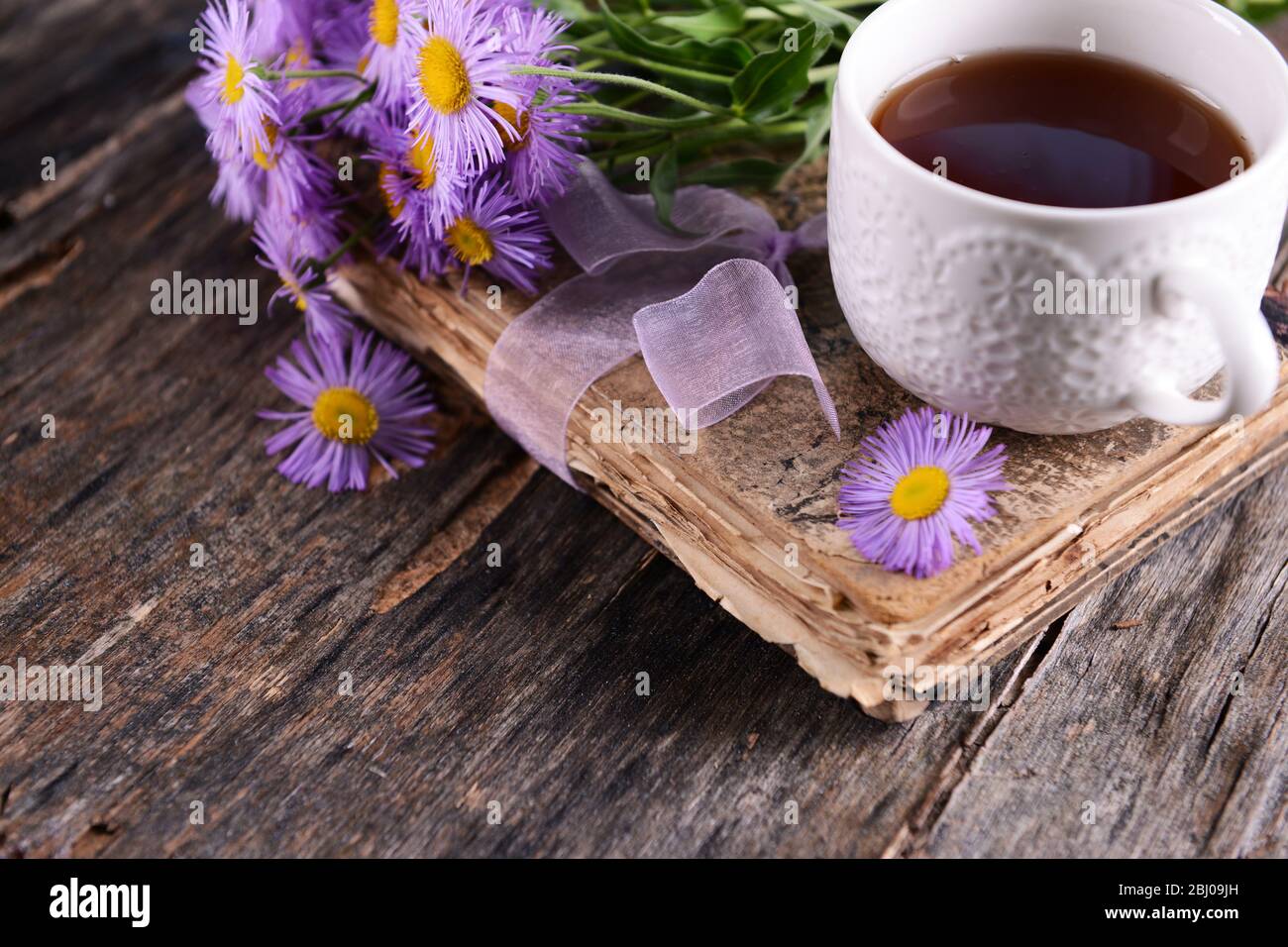Old book with beautiful flowers and cup of tea on wooden table close up Stock Photo