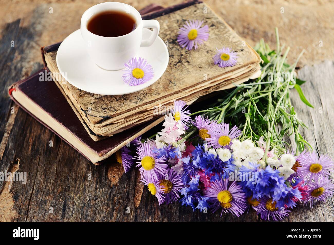 Old books with beautiful flowers and cup of tea on wooden table close up Stock Photo