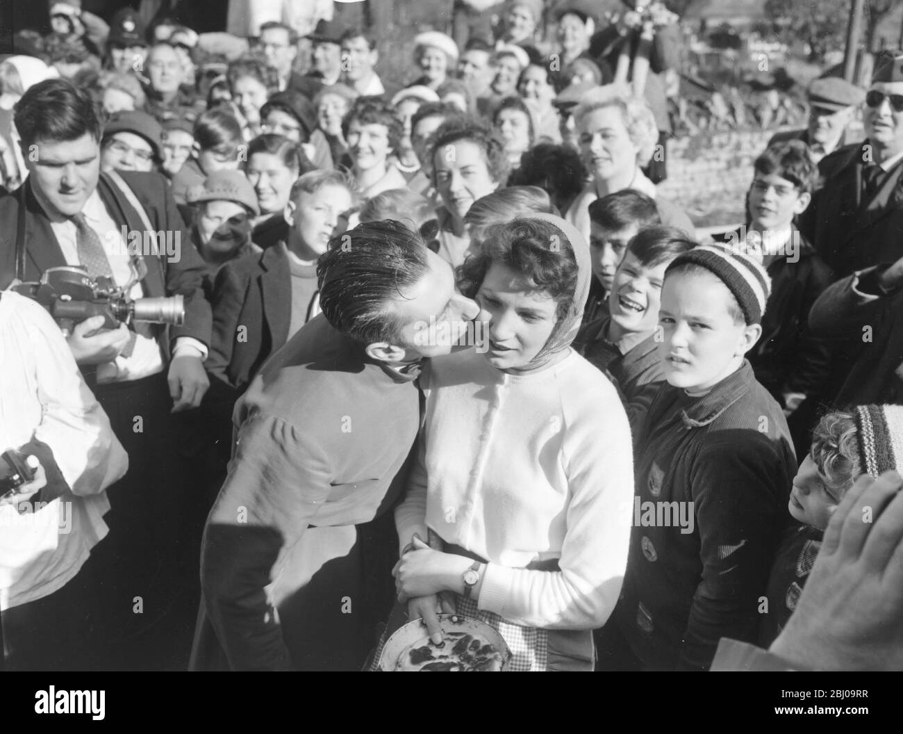 14 FEBRUARY 1961 - CAROL VORLEY - 19 YEAR OLD WINNER OF THE OLNEY PANCAKE RACE RECEIVES A KISS AT THE FINISHING LINE AFTER COMPLETING THE 415 YARD COURSE IN 1 MINUTE AND 14 SECONDS. THE RACE DATES BACK TO 1445 AND WAS REVIVED BY THE LOCAL VICAR IN 1946. - OLNEY, BUCKINGHAMSHIRE, ENGLAND - Stock Photo