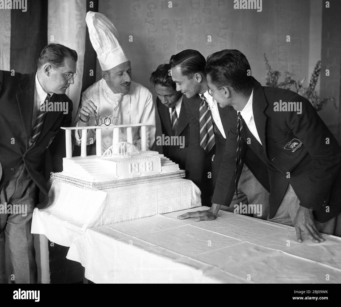 The Olympic Chef Presents ' Greek Theatre ' Cake to Ceylon Olympic Representatives - - When members of the Ceylon Olympic team moved into the Olympic Village at the Richmond , Surry , today Mr John Weier , the Olympic chef de cuisine at the camp , presented them with a cake made in the form of a Greek theatre . As soon as all the Ceylon competitors arrive the cake will be cut . - The chef and Ceylon Olympic members admiring the Olympiad 1948 cake at Richmond , Surrey today . Left to right , Mr Brant Little ( Ceylon Team Coach ) , Mr John Weider ( Olympic Chef De Cuisine ) Mr G . D Peiris ( lon Stock Photo