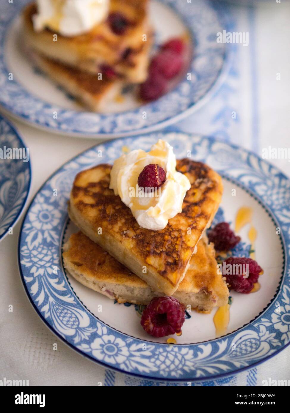 Pancakes made in heart shaped cutters served with whipped cream, raspberries and a drizzle of honey. Stock Photo