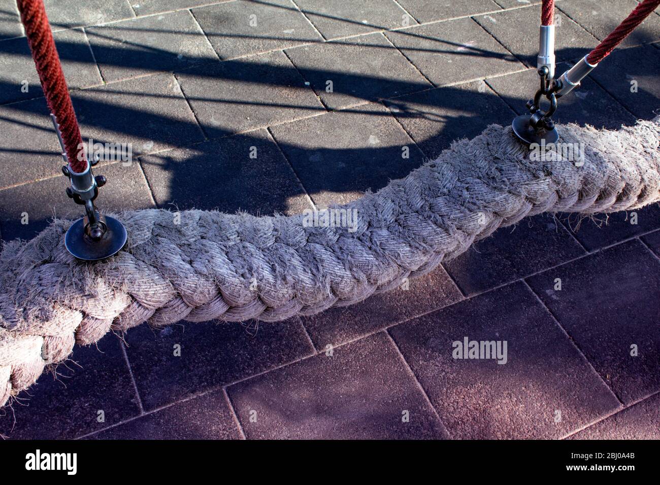 High angle view of an empty swing in a children's playground, made of thick polyester mooring rope, in shadows. Stock Photo