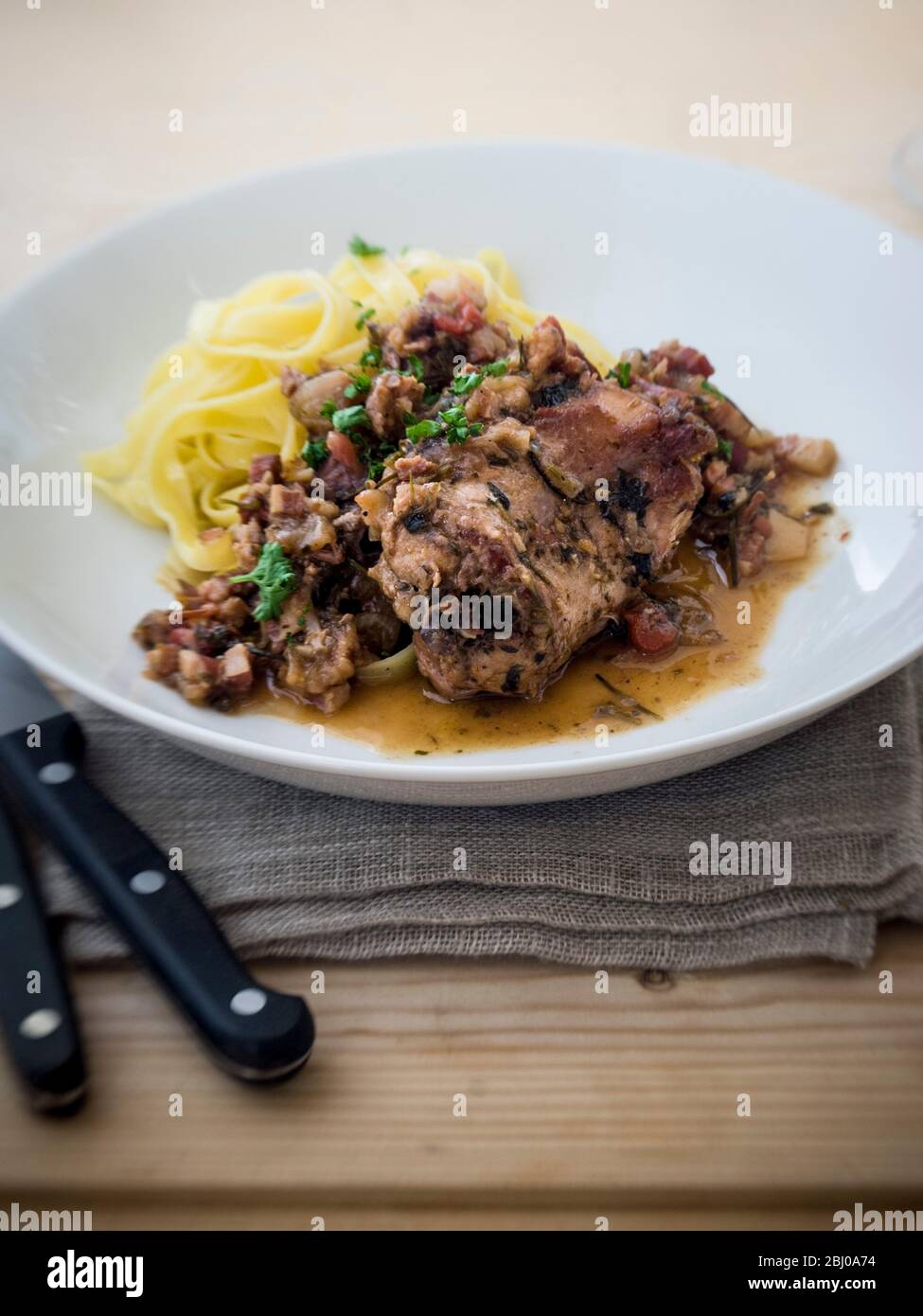 Saddle of rabbit cooked in wine and stock, with shallots, herbs and cherry tomatoes, served with noodles Stock Photo