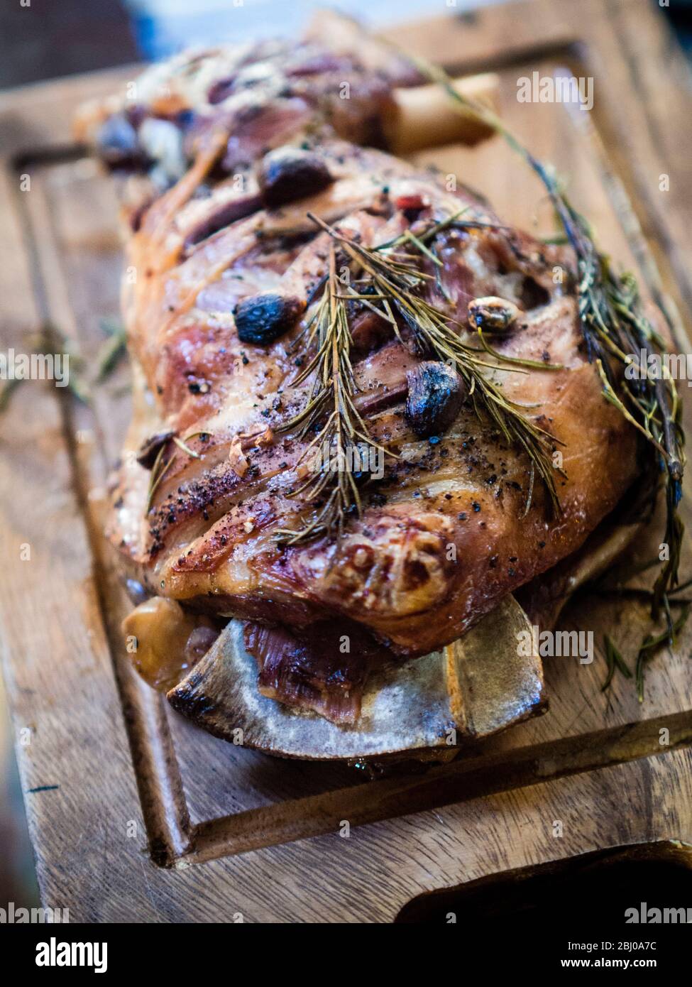 Slow roast shoulder of lamb with garlic and rosemary, on wooden carving board Stock Photo