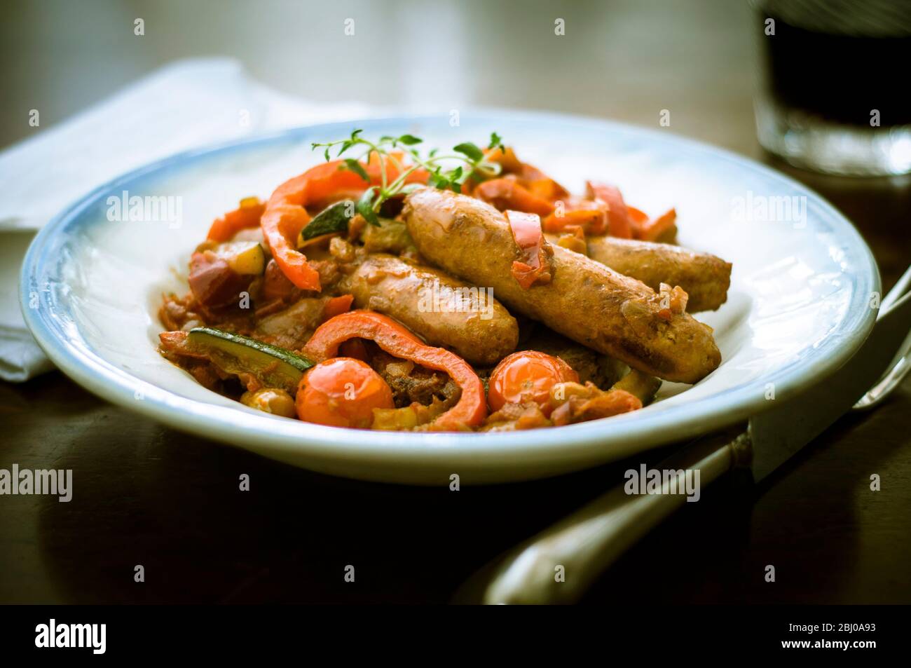 Spanish style dish of chorizo sausages with red peppers, tomatoes, courgettes and red wine sauce Stock Photo