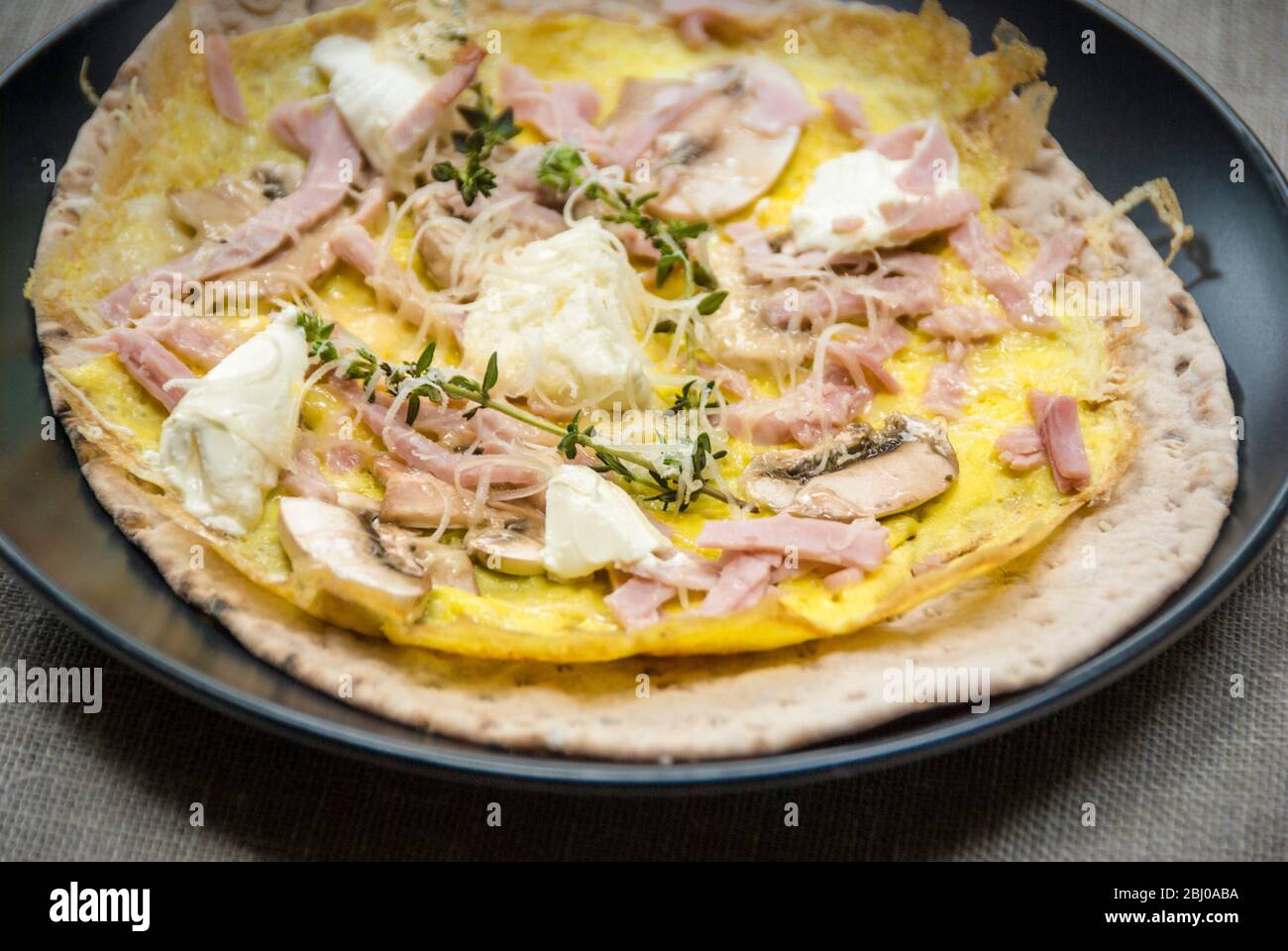 Thin pancake style omelette with mushroom, ham, goat's cheese and parmesan on thin Swedish bread before being rolled up, as a portable breakfast. Stock Photo