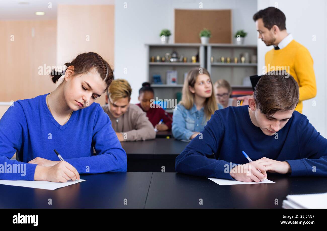 Serious positive teacher monitoring students’ work during examination test in class Stock Photo