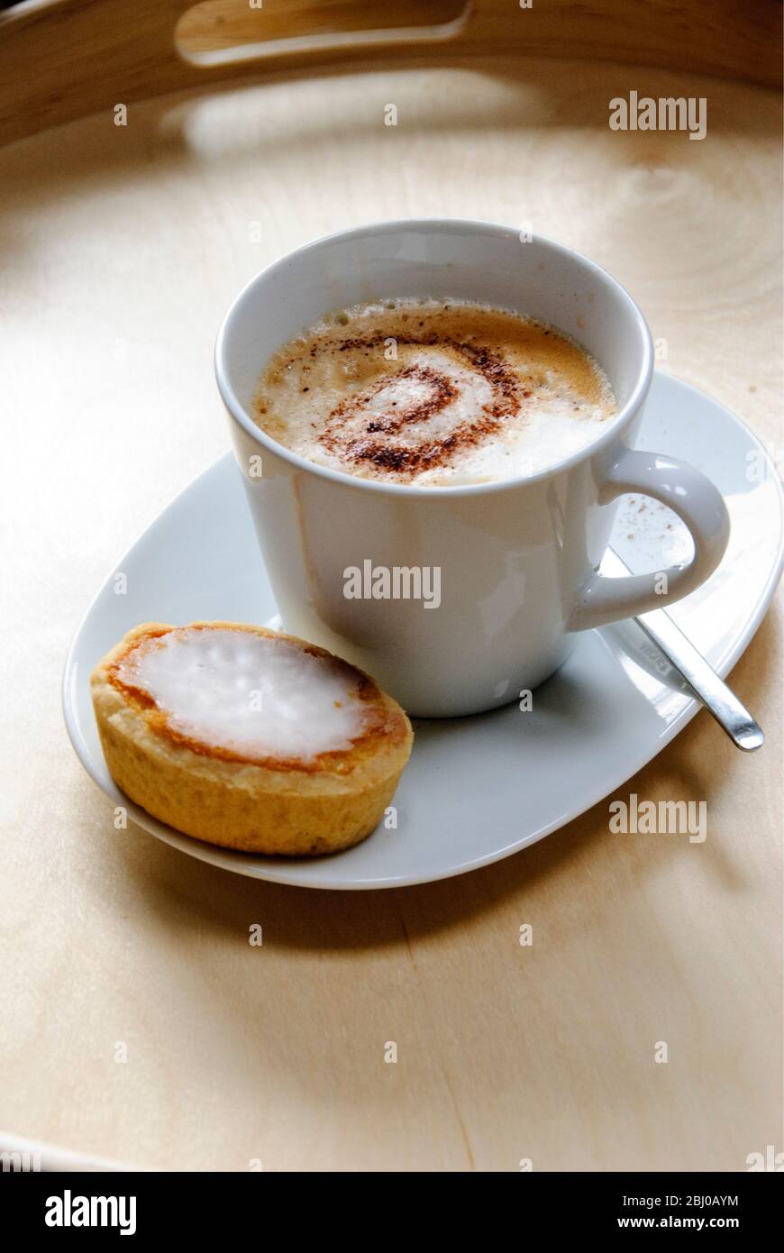Cup of cappuccino with spiral of cocoa dusted on top with Swedish almond tart - Stock Photo