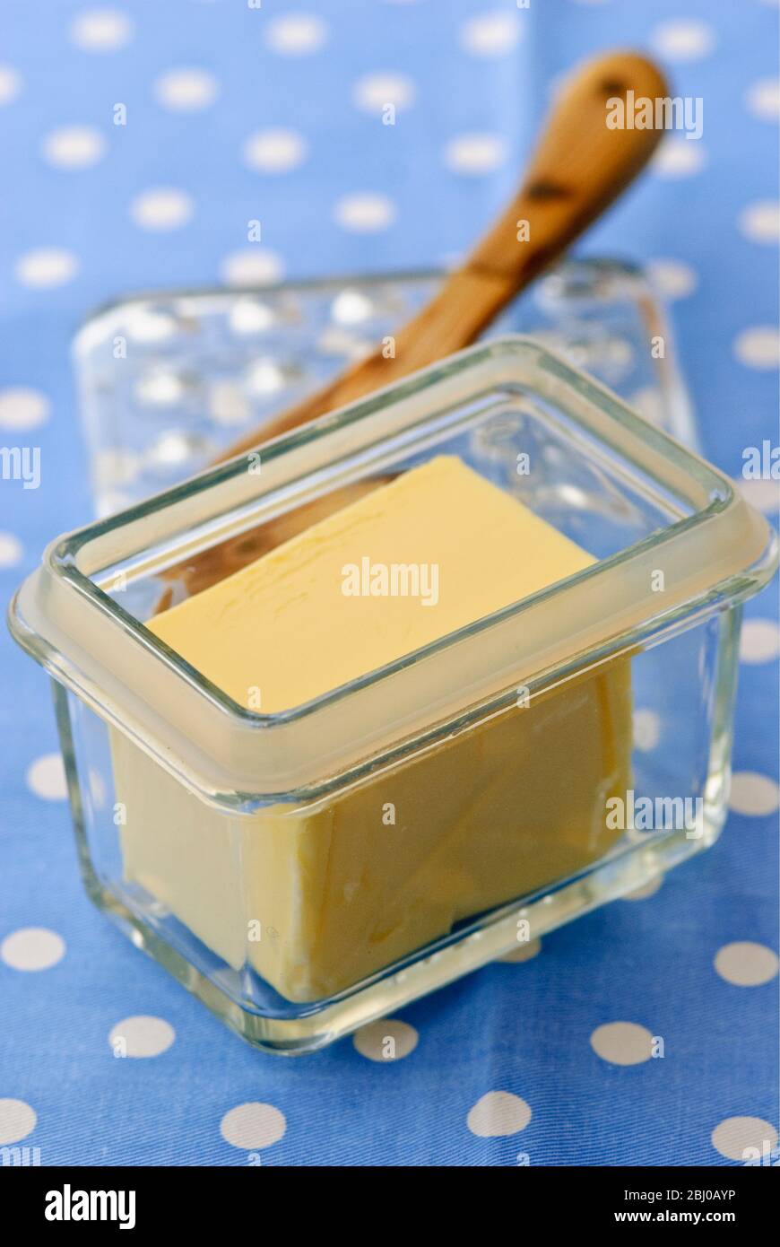 Glass butter dish of butter with butter knife on blue and white spotted cloth - Stock Photo