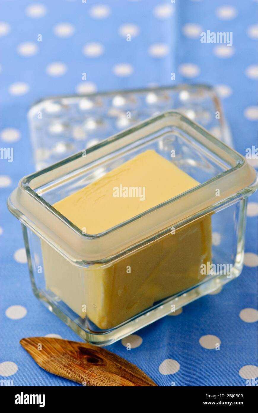 Glass butter dish of butter with butter knife on blue and white spotted cloth - Stock Photo