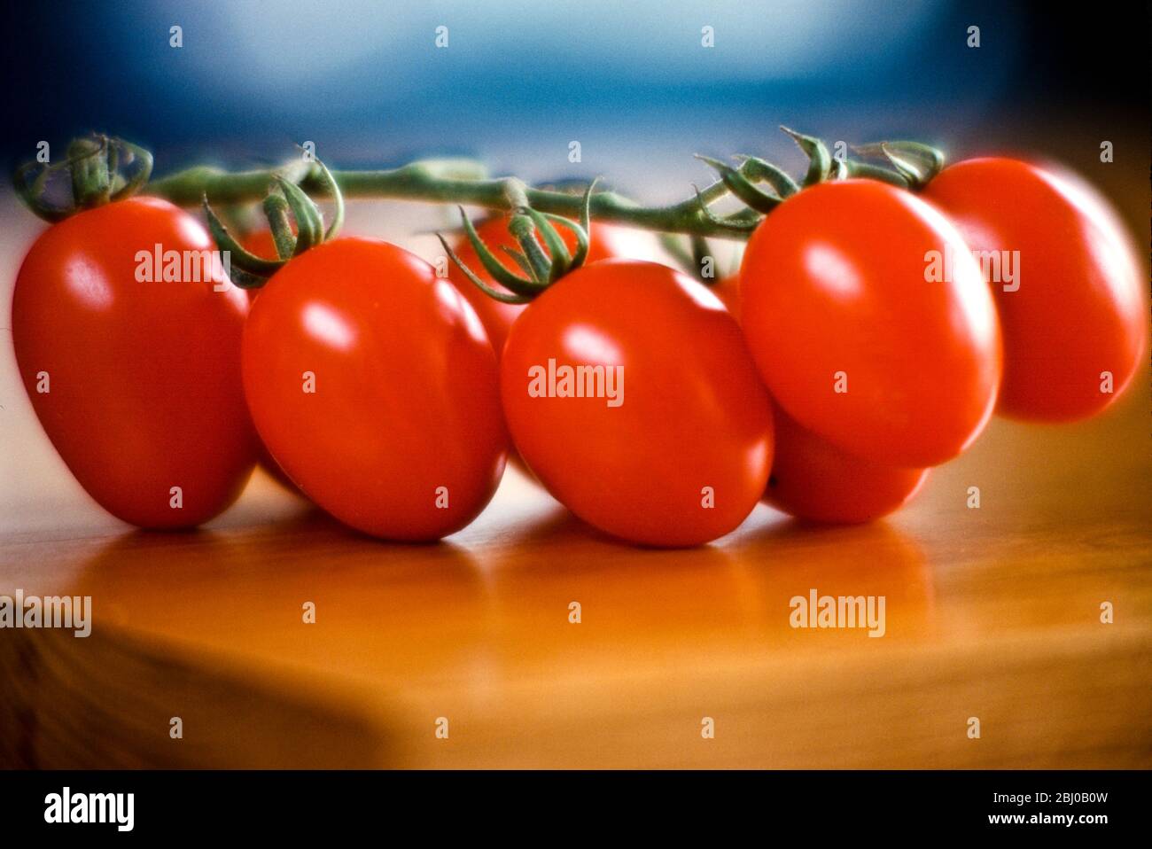 Cluster of shiny red plum tomatoes on the vine on wooden table surface - Stock Photo