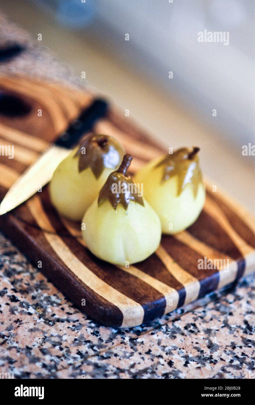 Peeled pears poached in vanilla sugar syrup on striped wooden board - Stock Photo