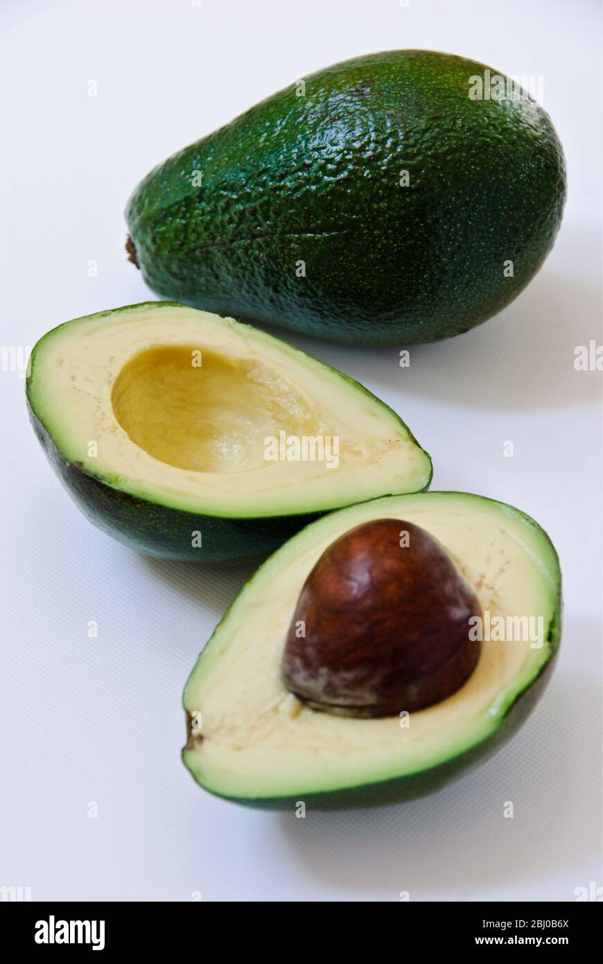 Whole and cut fresh avocado pear on white background - Stock Photo
