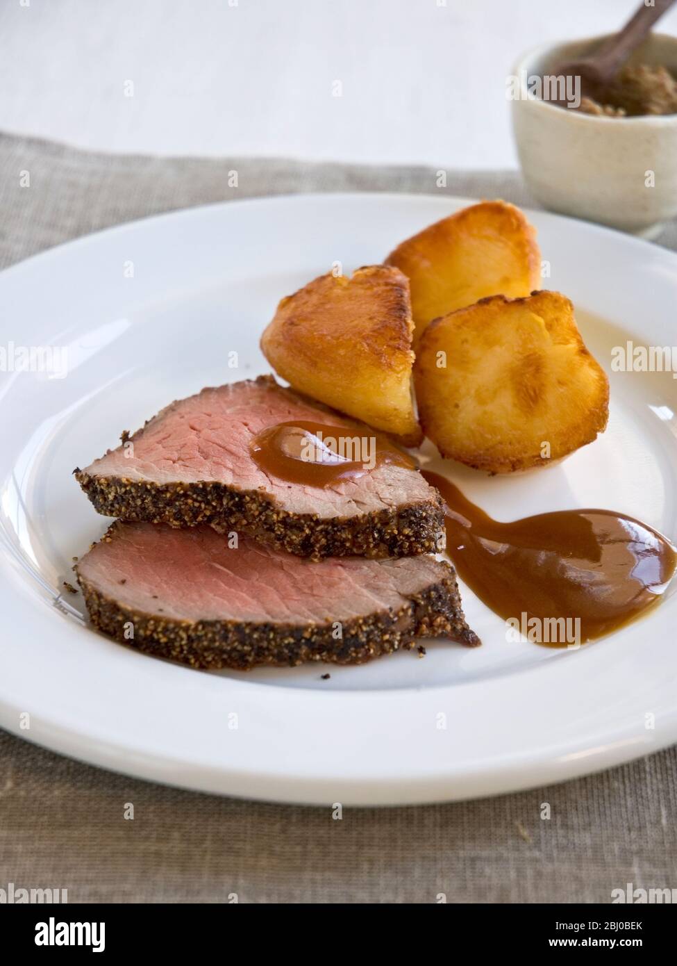 Slices of peppered roast fillet of beef with roast potatoes - Stock Photo