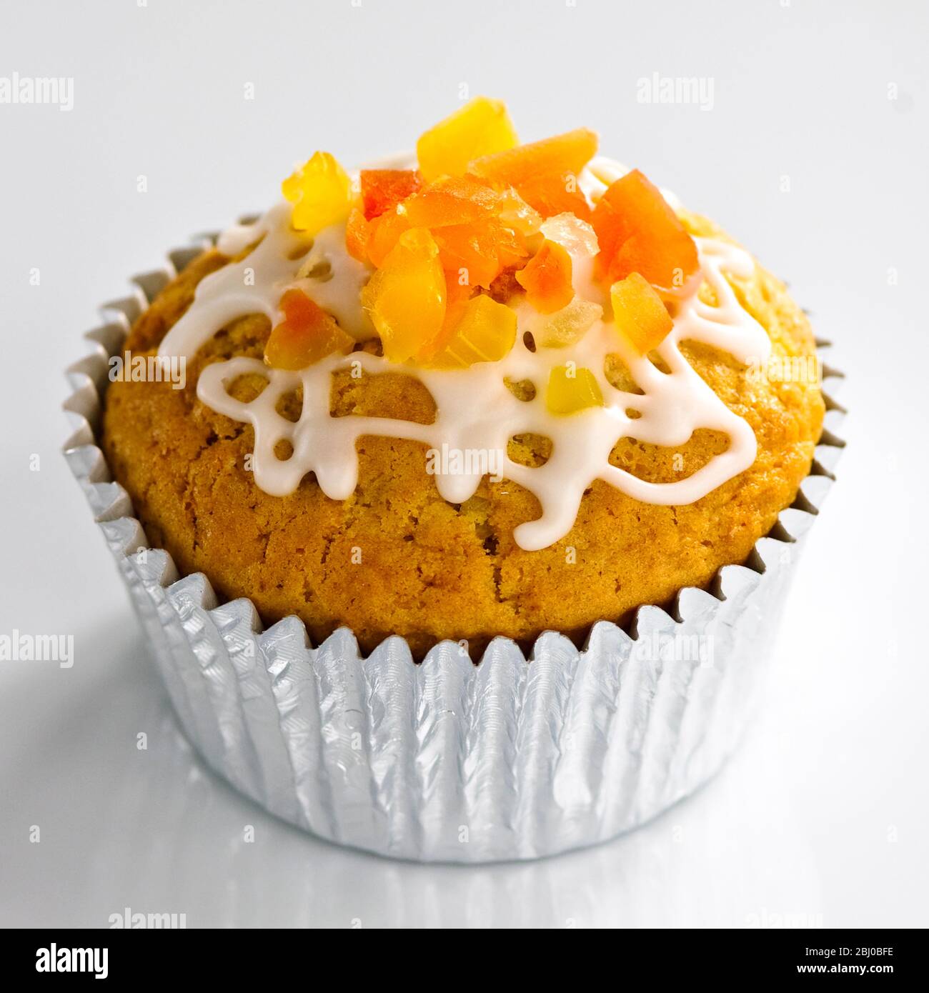 Sweet muffin in foilcase topped with candied fruit and icing trails - Stock Photo