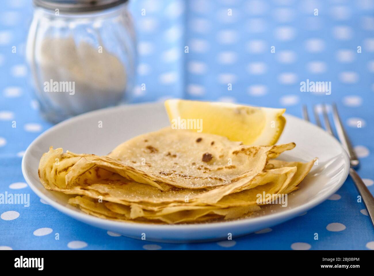 Pancakes folded in quarters with sugar dredged on and lemon wedge for squeezing - Stock Photo