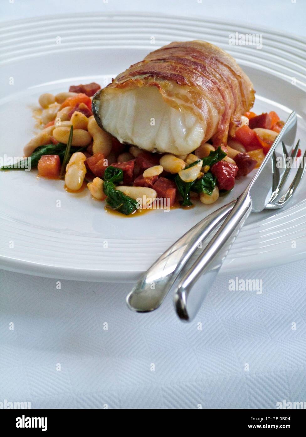 Roast monkfish loin wrapped in bacon on bed of bean cassserole - Stock Photo