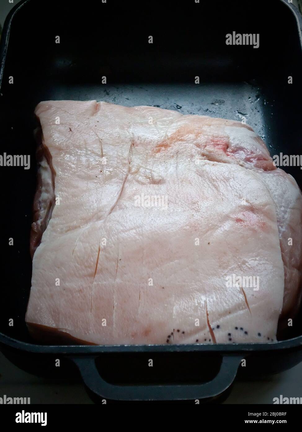 A piece of belly of pork ready for roasting in metal roasting tin - Stock Photo