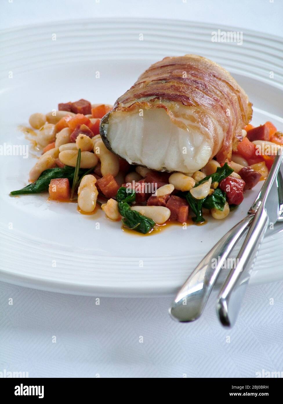 Roast monkfish loin wrapped in bacon on bed of bean cassserole - Stock Photo