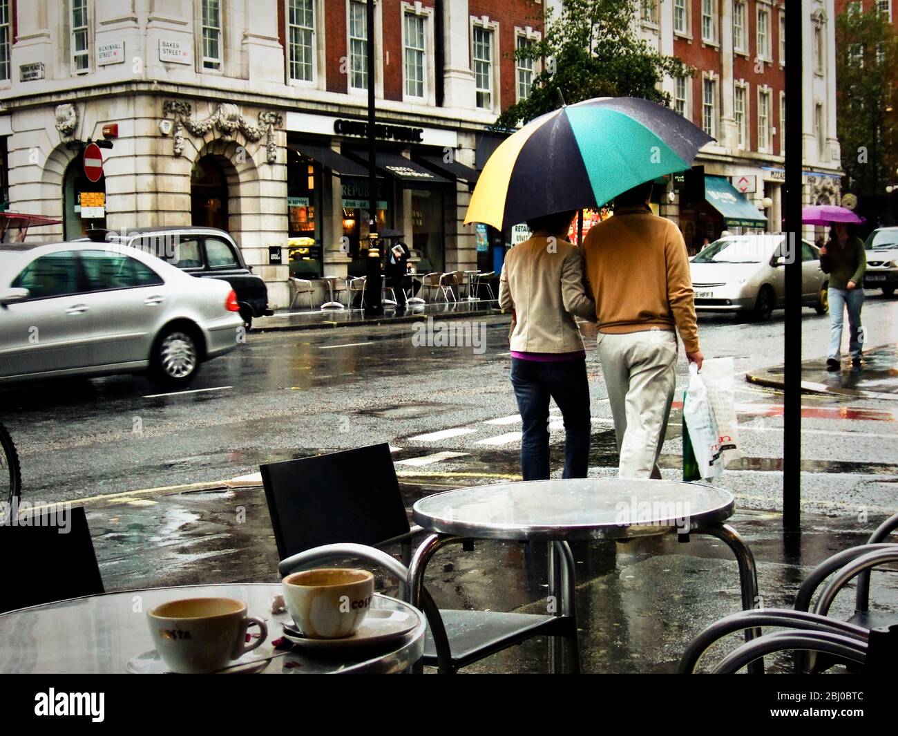 Street scene from London coffee shop with couple under golfing umbrella - Stock Photo