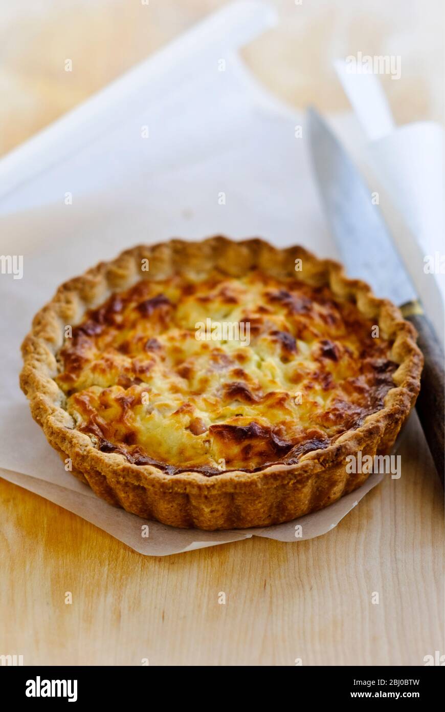 Little Quiche Lorraine on curled greaseproof paper with knife - Stock Photo