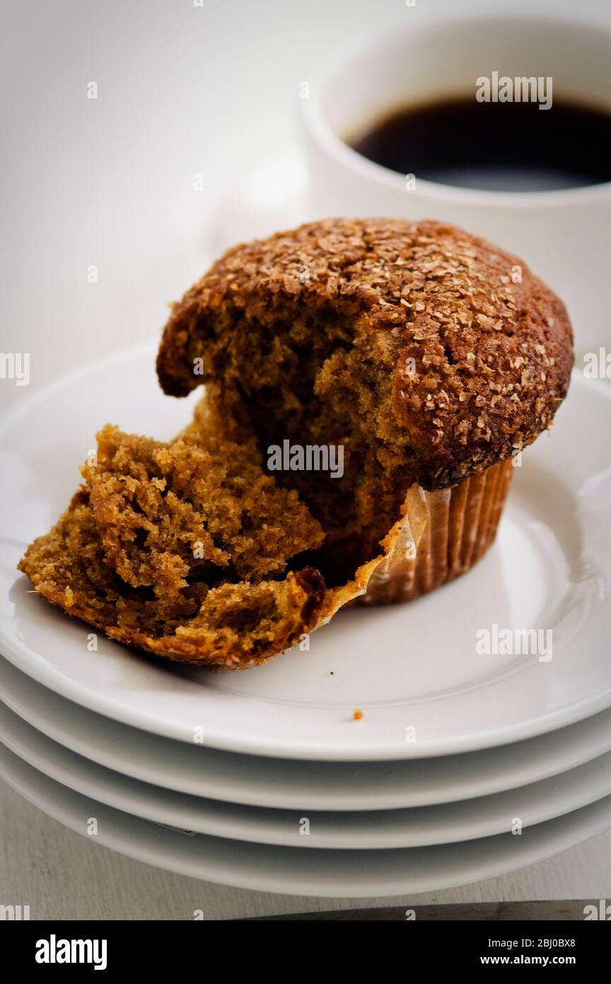 Cinnamon bran muffin on stack of white plates with cup of black coffee - Stock Photo