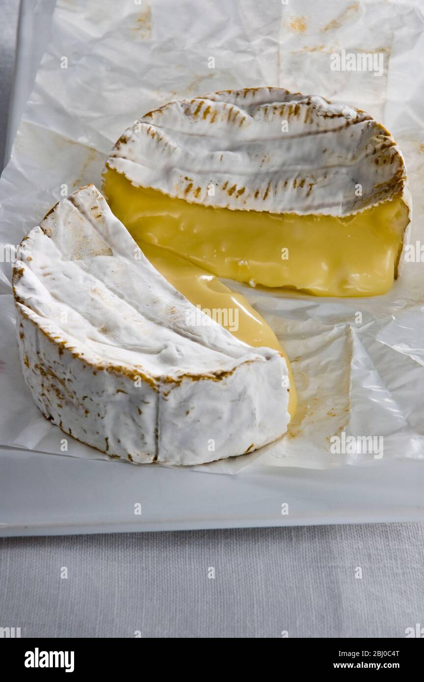 Whole round Camembert cheese cut in half showing ripe runny interior - Stock Photo