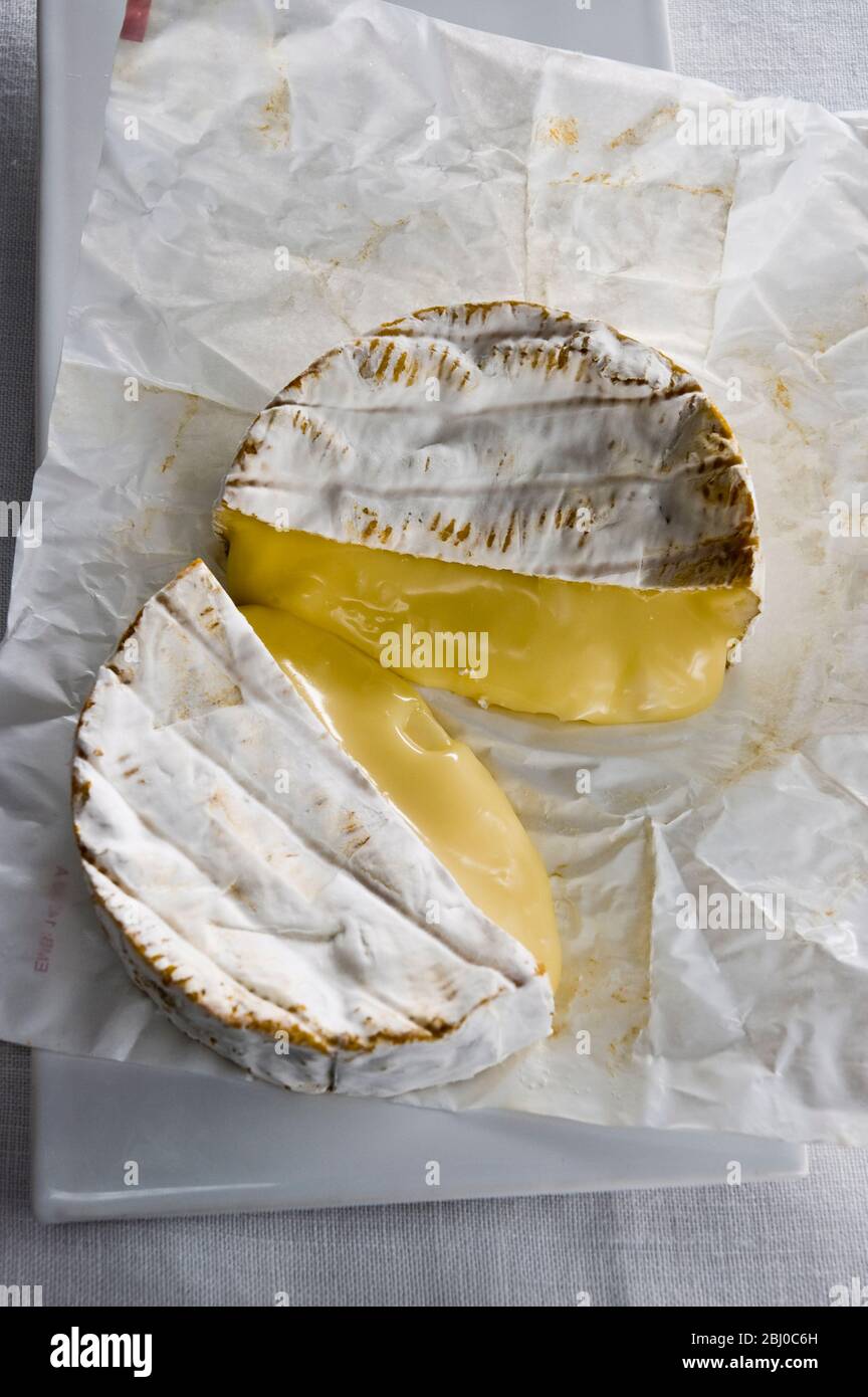 Whole round Camembert cheese cut in half showing ripe runny interior - Stock Photo