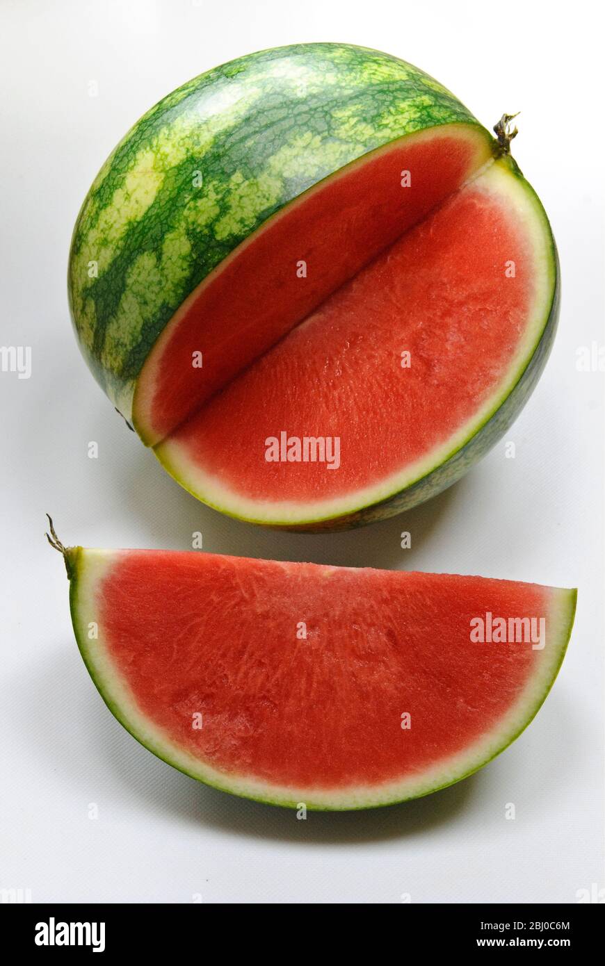 Small watermelon on white surface with quarter cut out showing red flesh - Stock Photo