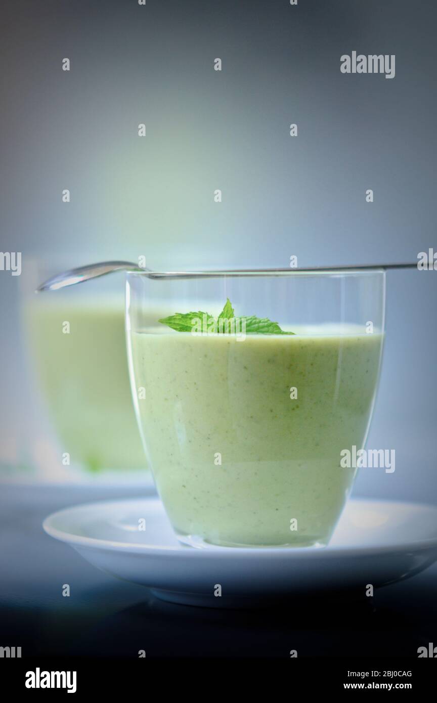 Chilled soup of fresh garden peas and courgettes in small glasses on white saucers with mint sprig garnish, made with garlic, onions, rosemary and yog Stock Photo
