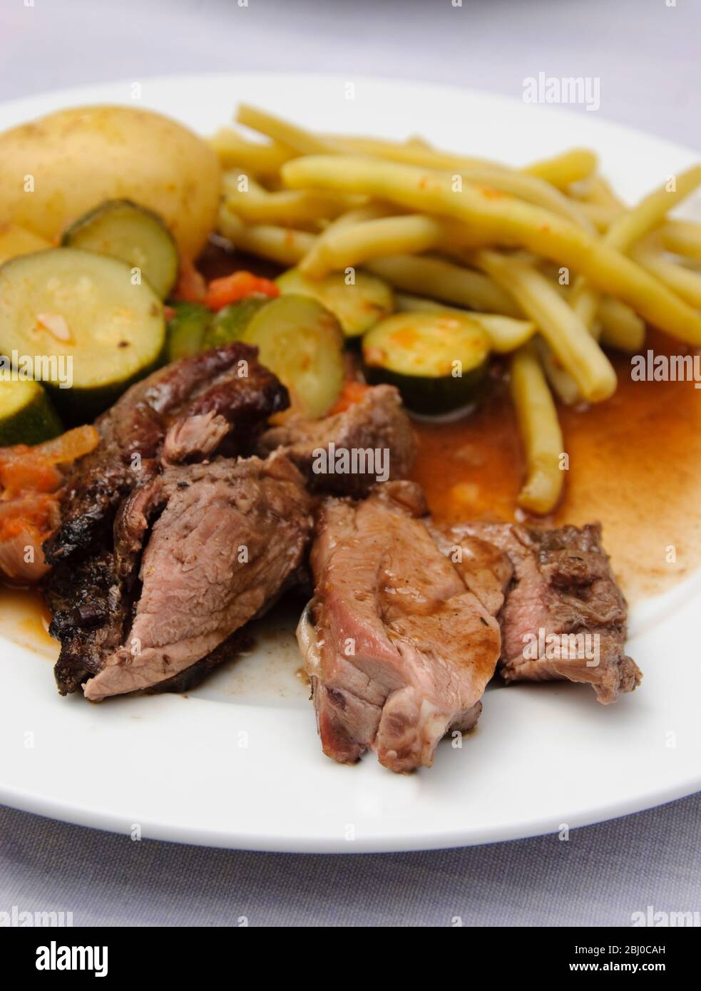 Lunch outdoors, of barbecue roast butterflied leg of lamb, with ratatouille and yellow wax pod beans - Stock Photo