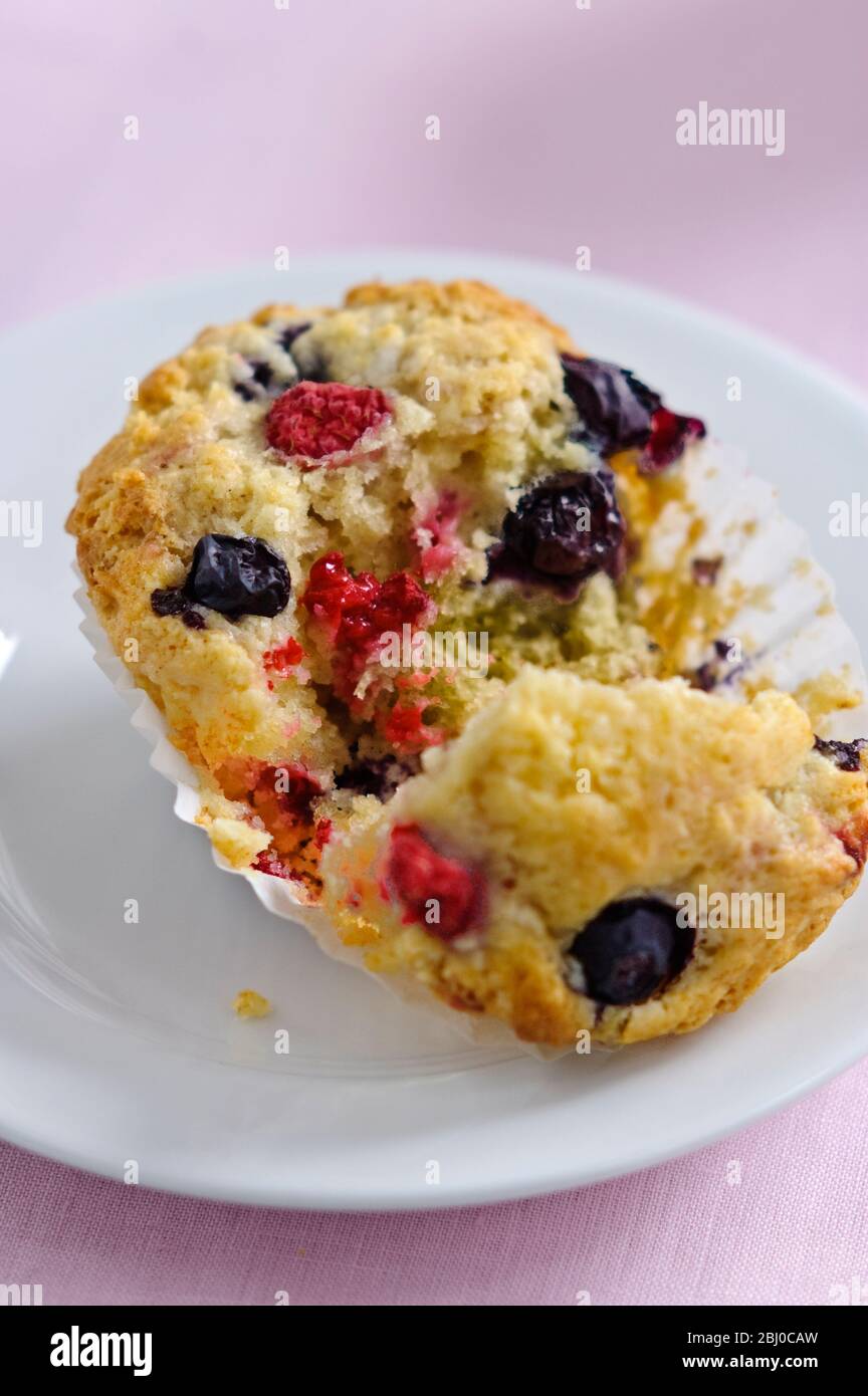 Berry muffin, broken open on white plate - Stock Photo
