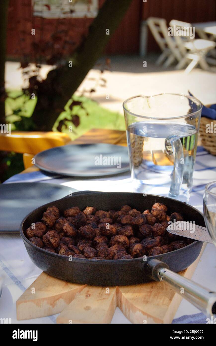 Frying pan of Swedish meatballs on table outside in dappled summer sunshine - Stock Photo
