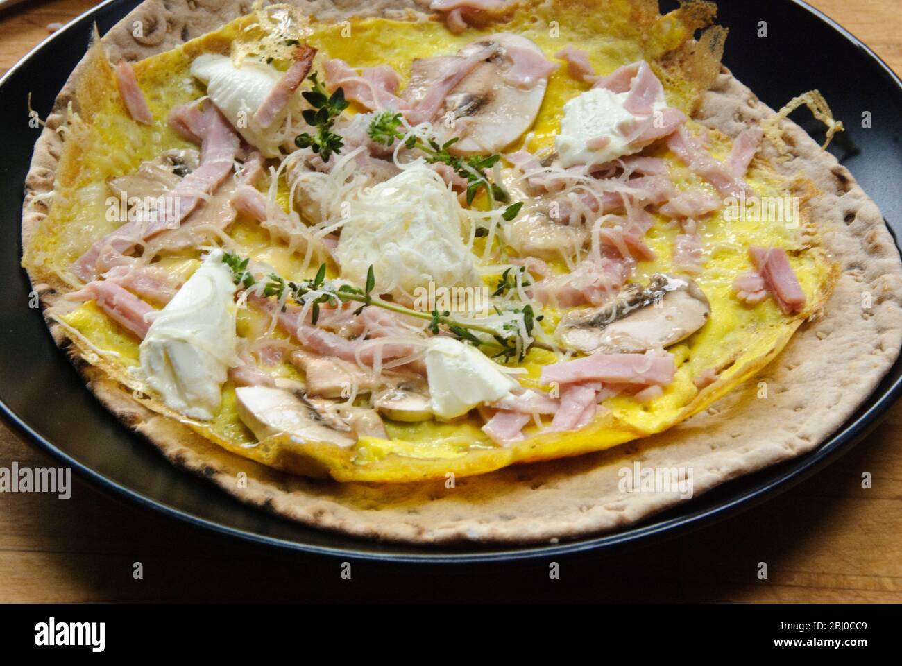 Thin pancake style omelette with mushroom, ham, goat's cheese and parmesan on thin Swedish bread before being rolled up, as a portable breakfast. - Stock Photo