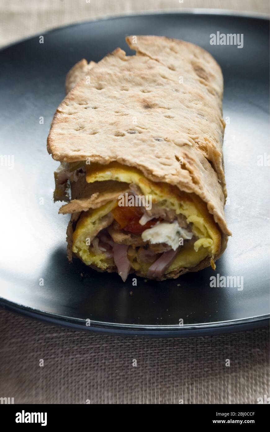 Thin pancake style omelette with mushroom, ham, sundried tomatoes, goat's cheese and parmesan on thin Swedish bread rolled up, as a portable breakfast Stock Photo