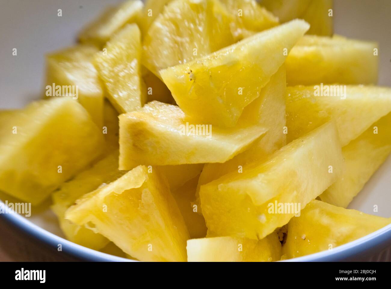 Freshly cut pieces of whole pineapple in white bowl - Stock Photo