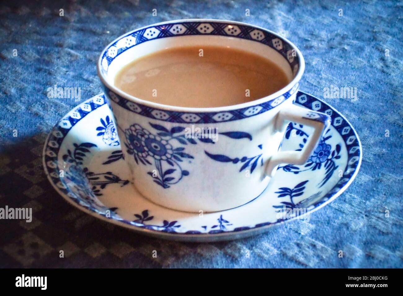 Antique blue and white cup and saucer of Indian tea with milk, on blue tablecloth - Stock Photo
