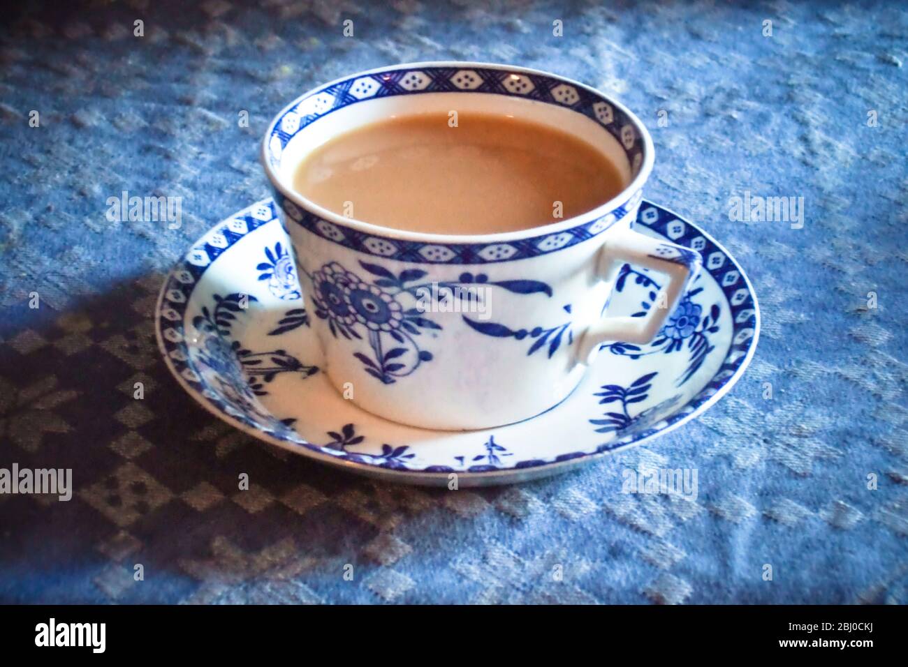 Antique blue and white cup and saucer of Indian tea with milk, on blue tablecloth - Stock Photo